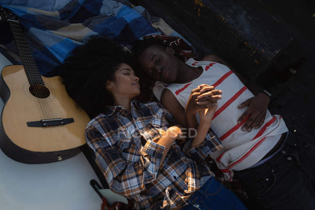 Высокоугольный вид молодой афроамериканской пары, лежащей в машине возле гитары на пляже в солнечный день — стоковое фото