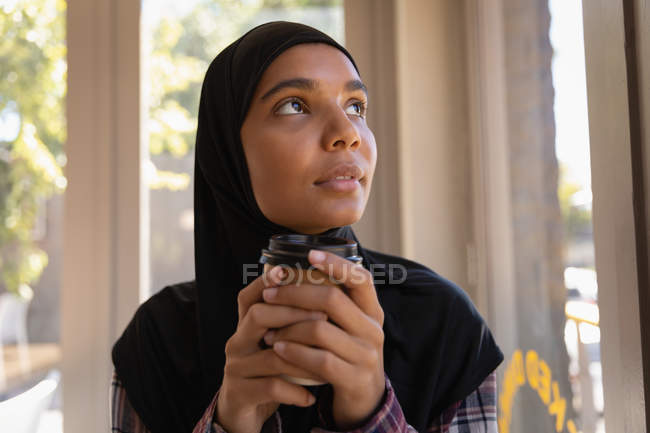 Front view of thoughtful young woman in hijab having coffee in a cafe — Stock Photo