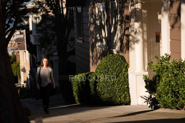 Вид спереди женщины, идущей по улице в солнечный день — стоковое фото