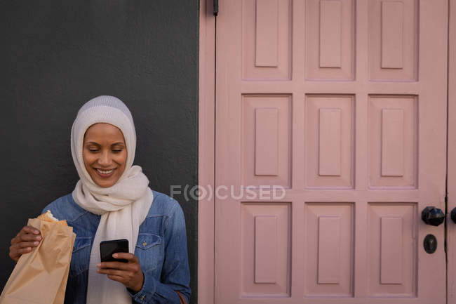Vista frontal de uma mulher mestiça feliz usando seu telefone celular enquanto toma café da manhã na rua — Fotografia de Stock