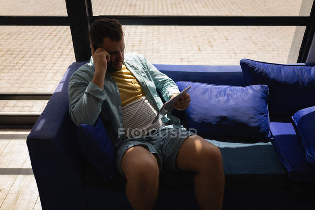 Vista de alto ângulo do homem caucasiano usando tablet digital no sofá azul em uma oficina — Fotografia de Stock