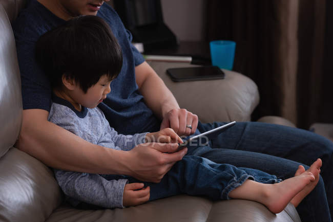 Вид сбоку отца-азиата и его сына, сидящих дома на диване с цифровым планшетом — стоковое фото