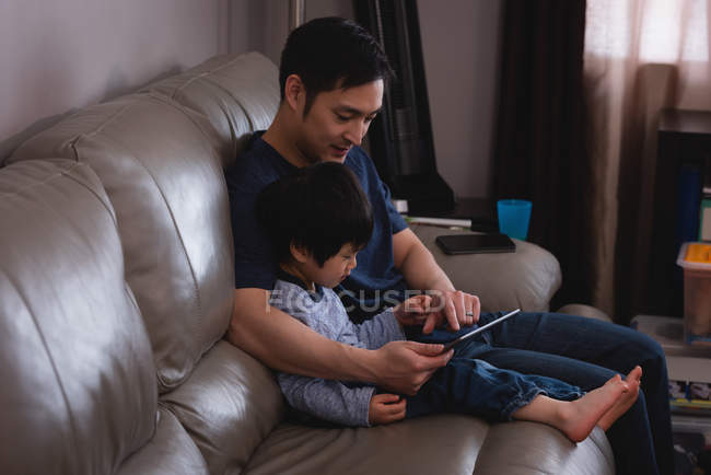 Вид збоку азіатського батька і його сина за допомогою цифрової таблетки, сидячи на дивані вдома — стокове фото