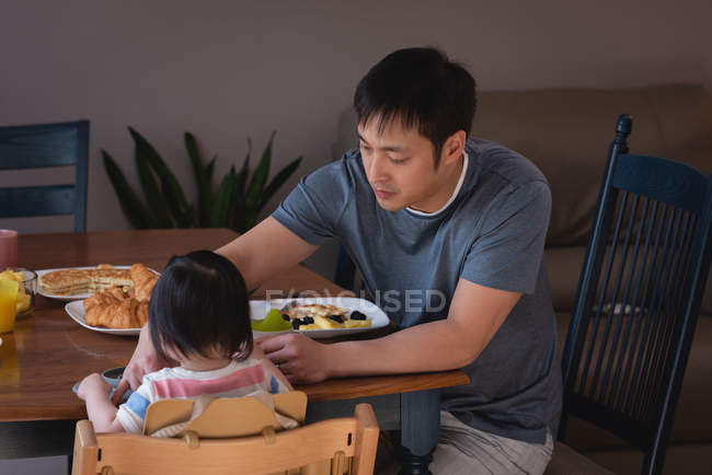 Vorderansicht eines asiatischen Vaters, der seine Tochter zu Hause am Esstisch in der Küche füttert — Stockfoto