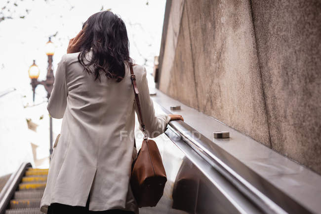 Rückansicht einer asiatischen Frau, die auf der Rolltreppe mit dem Handy telefoniert — Stockfoto