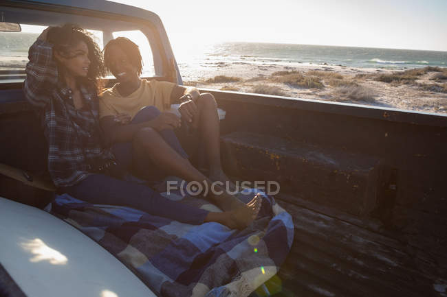 Вид сбоку на молодую афроамериканскую пару, взаимодействующую друг с другом, сидя в машине на пляже в солнечный день — стоковое фото