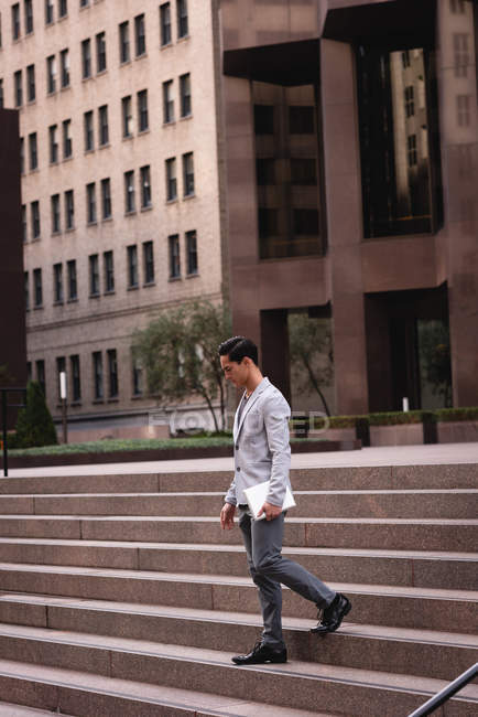 Vista lateral de homem asiático bonito andando da escada enquanto segurando tablet digital — Fotografia de Stock
