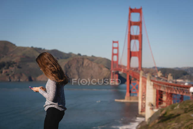 Вид сбоку женщины, пользующейся мобильным телефоном, стоя на склоне горы — стоковое фото
