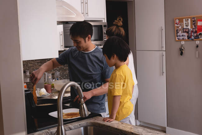 Vista lateral de padre asiático enseñando hijo a hacer panqueques en la cocina en casa - foto de stock