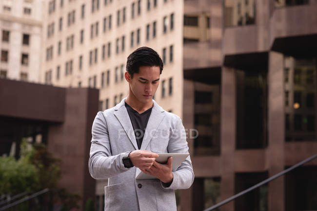 Vista frontale di bello asiatico uomo utilizzando tablet digitale mentre in piedi sulla strada — Foto stock