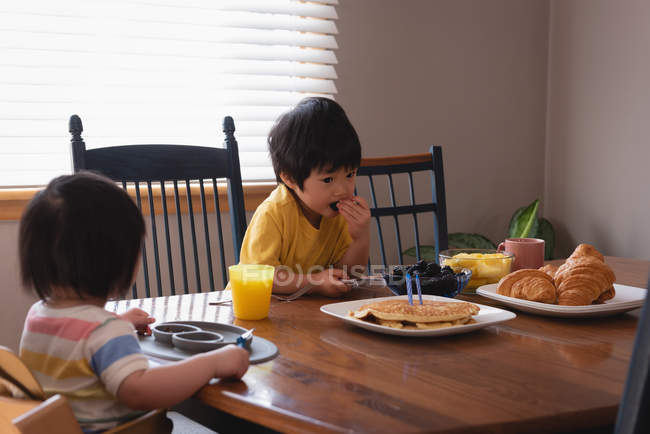 Vista frontal de crianças asiáticas tomando café da manhã enquanto se sentam na mesa de jantar na cozinha em casa — Fotografia de Stock
