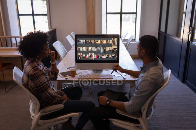 Side view of young Mixed-race graphic designers discussing with each other over computer at desk in office where appear pictures — Stock Photo