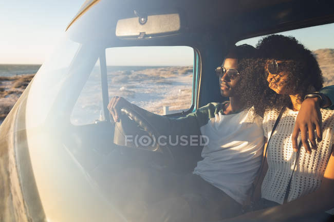 Vista frontal do romântico jovem casal afro-americano relaxando em um carro em um dia ensolarado — Fotografia de Stock