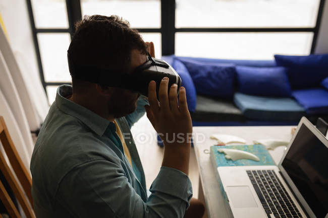 Vista lateral do homem caucasiano usando fone de ouvido enquanto sentado na frente do laptop na oficina — Fotografia de Stock