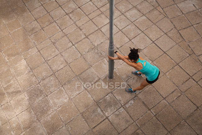 Vista de alto ângulo da jovem mulher de raça mista ouvindo música em fones de ouvido enquanto se exercita na cidade — Fotografia de Stock