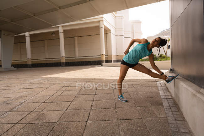 Side view of young Mixed race woman listening music on earphones while exercising in the city — Stock Photo