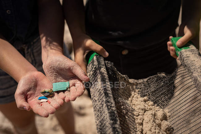 Mid section of volunteers holding waste in hand at beach on a sunny day — Stock Photo