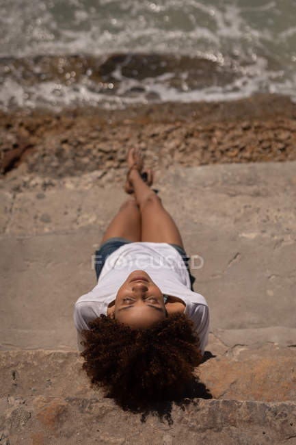 Вид под высоким углом на молодую симпатичную женщину смешанной расы, отдыхающую на пляже в солнечный день — стоковое фото