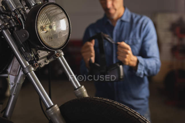 Primer plano de la luz de la cabeza de la bicicleta con mecánico de bicicleta masculino en el fondo en el garaje - foto de stock