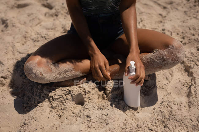 Baixa seção de mulher com protetor solar loção relaxante na praia — Fotografia de Stock