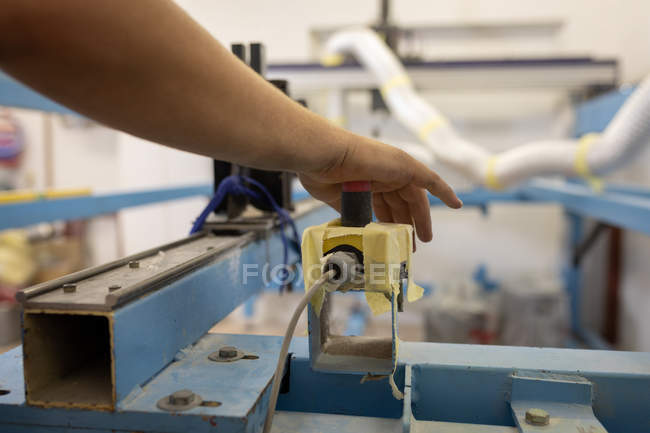 Primer plano del trabajador presionando el botón rojo de la máquina en el taller de tabla de surf - foto de stock