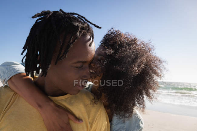Вид спереди на молодую романтическую афроамериканскую пару, стоящую с рукой на пляже в солнечный день — стоковое фото