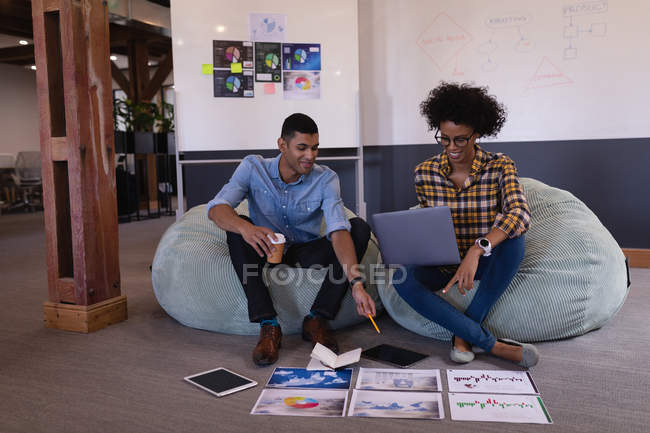 Первый взгляд на счастливых молодых бизнесменов смешанной расы, обсуждающих график сидя в современном офисе — стоковое фото