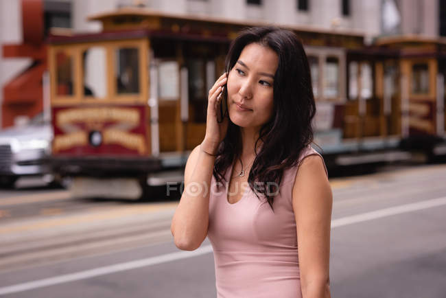Vorderansicht einer nachdenklichen Asiatin, die auf der Straße mit dem Handy telefoniert — Stockfoto