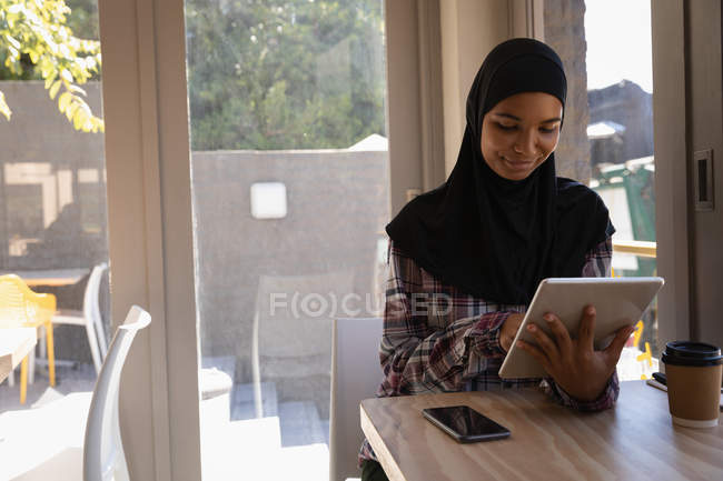 Вид спереди красивой молодой женщины в хиджабе с помощью цифрового планшета в кафе — стоковое фото