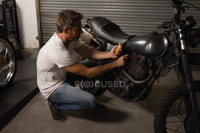 Vista lateral de la bicicleta masculina caucásica chequeo mecánico batería de bicicleta con multímetro en el garaje - foto de stock
