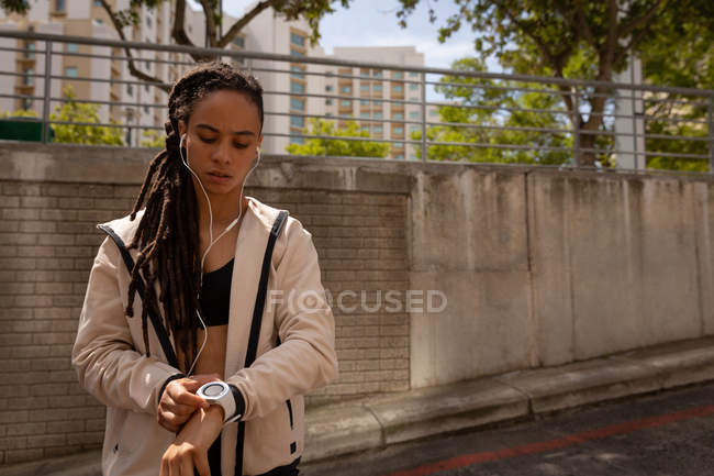Vista frontale della giovane donna di razza mista utilizzando smartwatch sulla strada della città — Foto stock