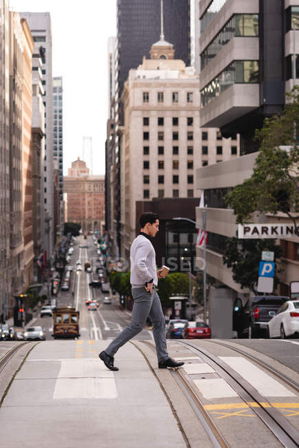 Seitenansicht eines asiatischen Mannes, der beim Kaffee die Straße überquert — Stockfoto