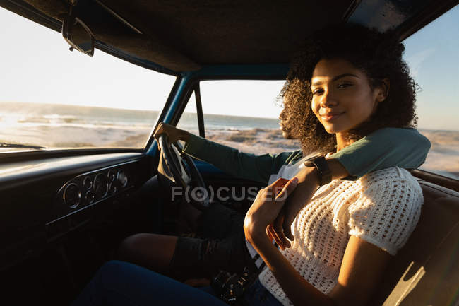 Vista lateral de pareja afroamericana joven y romántica relajándose en un coche en un día soleado - foto de stock