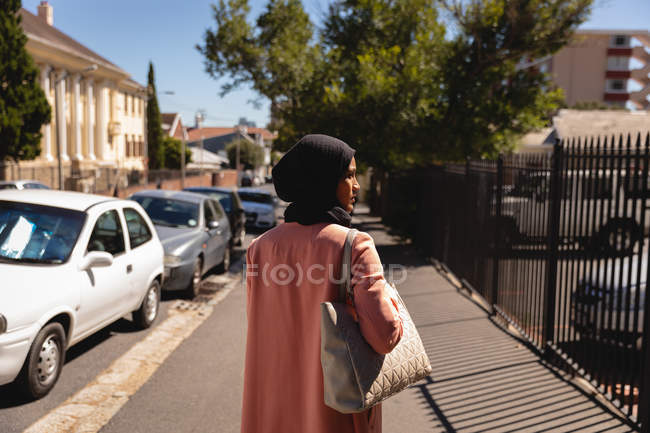 Вид ззаду вдумлива змішана жінка, що стоїть на вулиці в сонячний день — стокове фото