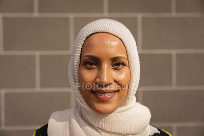 Portrait of a young mixed-race woman smiling to the camera while standing in front of brick wall — Stock Photo