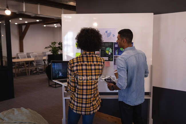 Взгляд сзади на молодых бизнесменов смешанной расы, взаимодействующих друг с другом по графику, стоящему в современном офисе — стоковое фото
