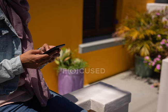 Metà sezione di donna utilizzando il telefono cellulare mentre seduto sul muro di fronte alla casa — Foto stock