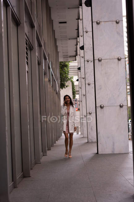 Font view of Asian woman talking on mobile phone while walking in corridor — Stock Photo