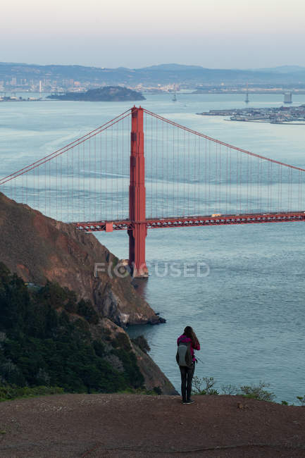 Vue arrière d'une femme prenant une photo d'un pont par une journée ensoleillée — Photo de stock