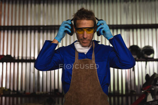 Front view of young Caucasian male bike mechanic listening music while working in garage — Stock Photo