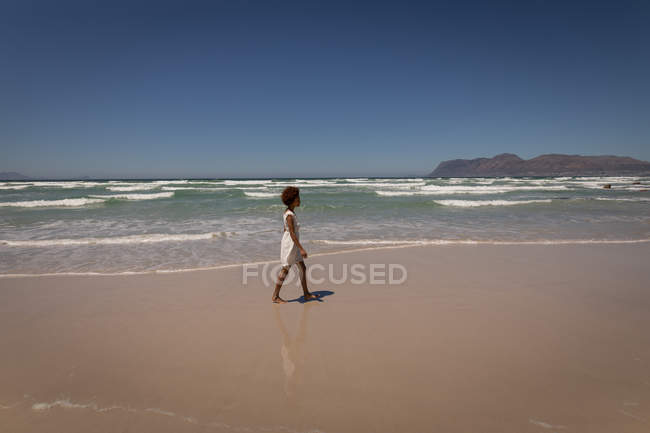 Вид сбоку красивой женщины смешанной расы, идущей одна по пляжу в солнечный день — стоковое фото