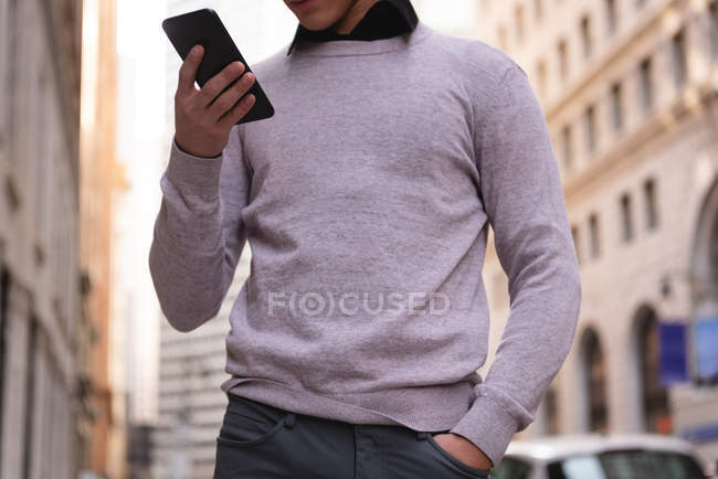 Средняя часть азиатского мужчины, стоящего на улице с помощью мобильного телефона — стоковое фото
