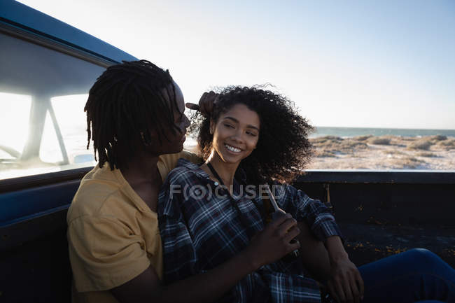 Вид сбоку счастливой афроамериканской пары, наслаждающейся, сидя в машине на пляже в солнечный день — стоковое фото