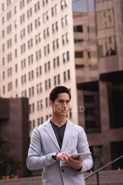 Vista frontal do homem asiático pensativo usando tablet digital enquanto está de pé na rua — Fotografia de Stock