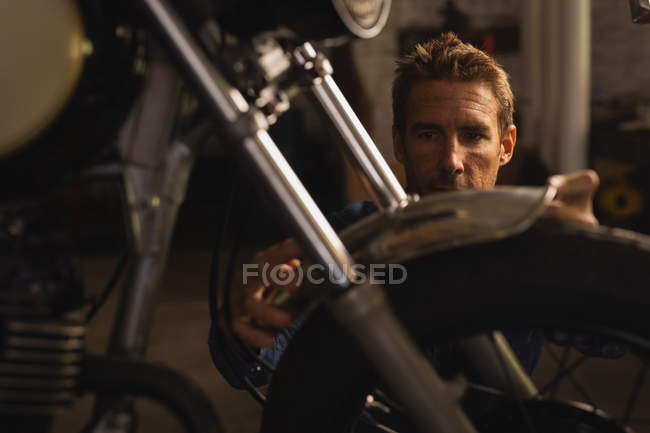 Front view of Caucasian male bike mechanic repairing mudguard of bike in garage — Stock Photo