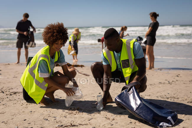 Vista frontal de voluntarios multiétnicos limpiando la playa en un día soleado - foto de stock
