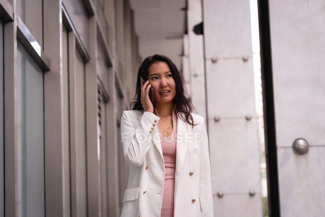 Vista frontale della donna asiatica che parla sul telefono cellulare mentre cammina in corridoio — Foto stock
