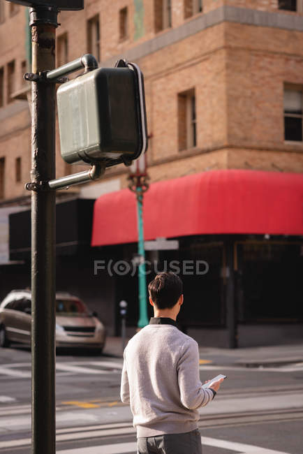 Vista posteriore di uomo asiatico tiene un telefono cellulare in attesa di attraversare la strada — Foto stock