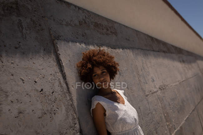 Portrait de jeune jolie femme métissée appuyée contre le mur à la plage par une journée ensoleillée — Photo de stock