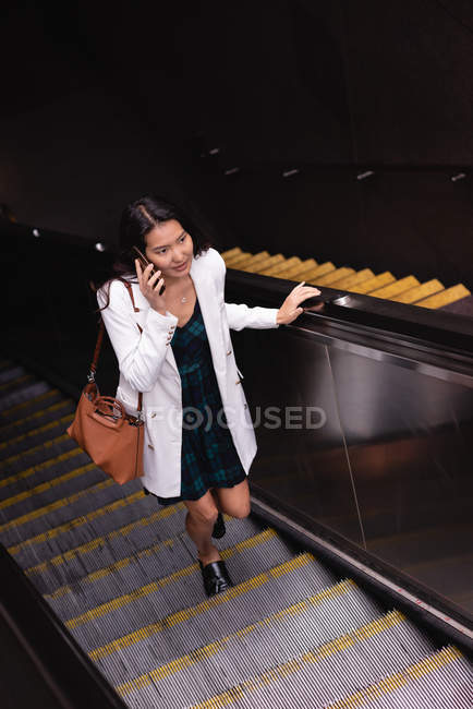 Hochwinkelaufnahme einer asiatischen Frau, die auf der Rolltreppe mit dem Handy spricht — Stockfoto